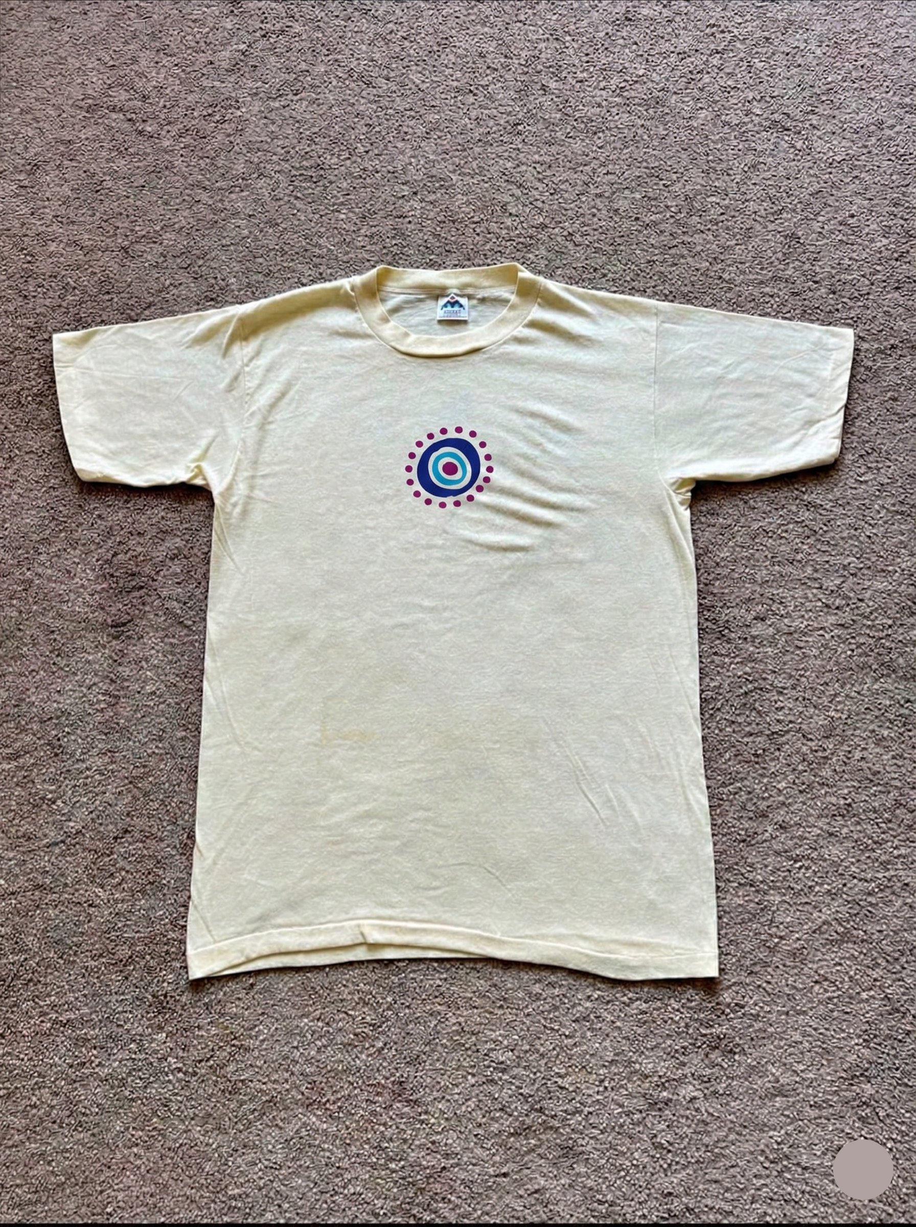 White t-shirt with a colorful circular design on a gray carpet